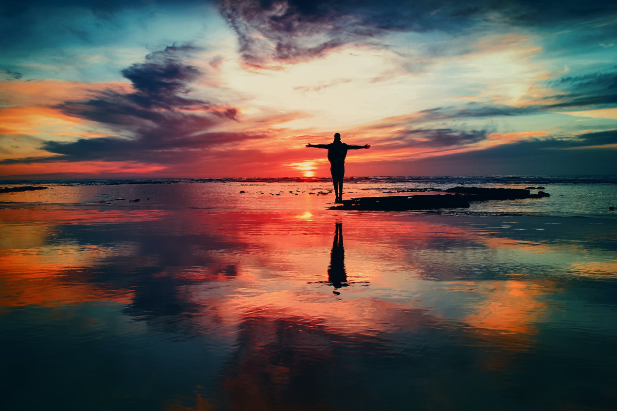 Egy férfi áll a tengerparton a megnyugtató, szivárványszínű naplementét nézve.